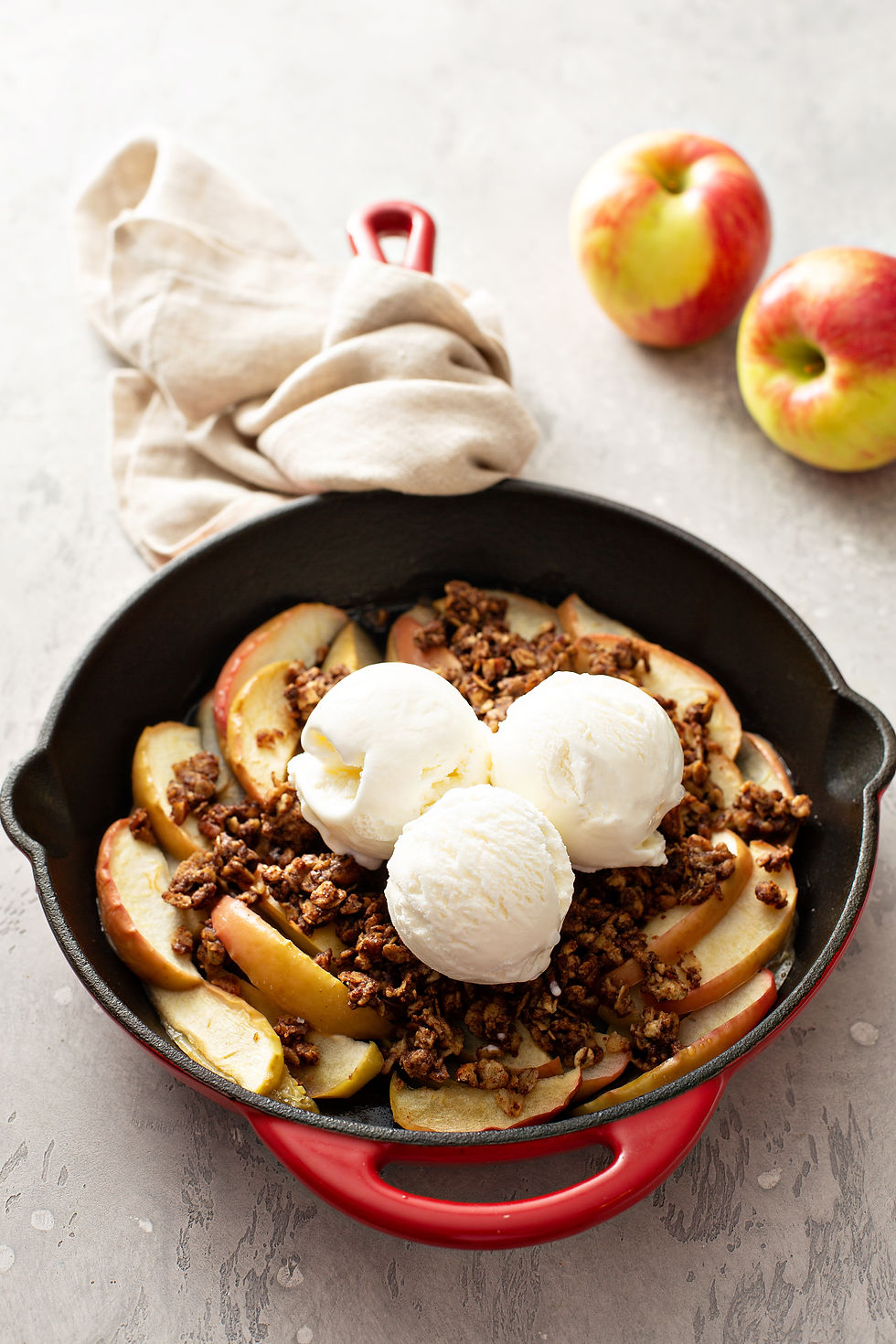 Bol de nachos inspirés du croustillant aux pommes avec des tranches de pommes Honeycrisp, du granola et des boules de crème glacée à la vanille, avec des pommes entières en arrière-plan.