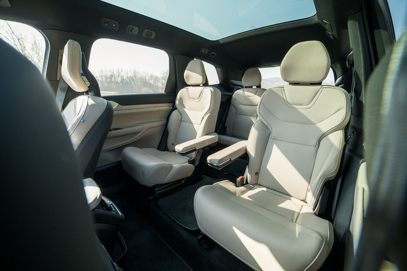 Blick in den Fond des Volvo EX90 Ultra Twin Motor 2026 mit zwei beigen Einzelsitzen in der zweiten Reihe und der dritten Sitzreihe dahinter, darüber das durchgehende Panoramaglasdach.