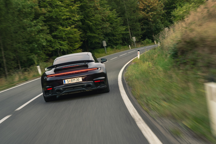 Porsche 911 Turbo S 992.1 2024 in Dunkelviolett auf kurviger Landstraße von hinten fotografiert