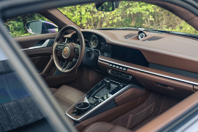 Innenraum des Porsche 911 Turbo S 992.1 mit braunem Leder, Sportlenkrad und modernem Cockpit.