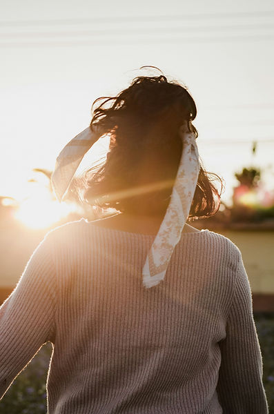 Woman sitting in soft sunlight, arms resting loosely, symbolizing pause, nervous system regulation, and attachment‑informed t