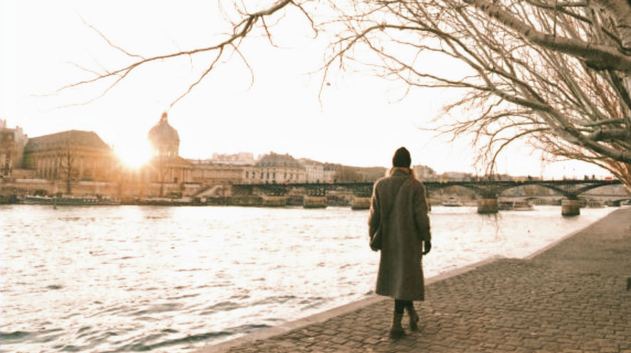 A lonely solo expat woman walks alone along the Seine river bank.