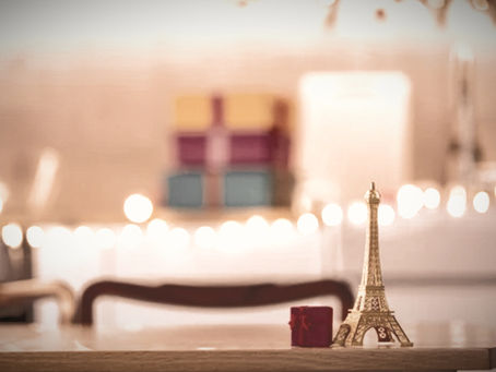 Small Eiffel Tower decoration and wrapped gift with holiday lights in the background, representing an expat Christmas season in France.