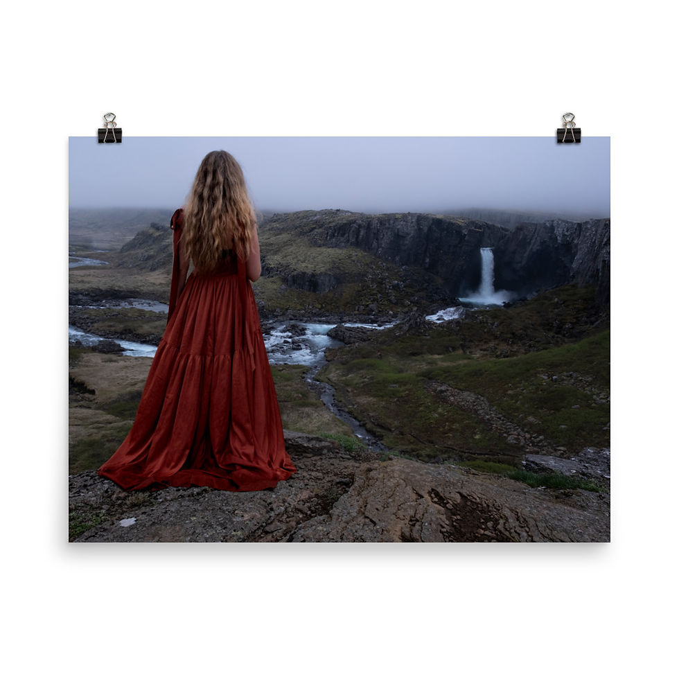 woman in red looking into the distance at a waterfall flowing through the Icelandic landscape