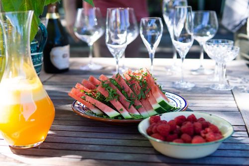 Table de jardin avec carafe de jus d'orange, pastèque et framboises, accord apéritif pour le cocktail Passion des îles du Domaine de La Garnaudière