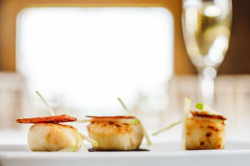 Amuse-bouches de saint-jacques avec une coupe de vin effervescent en arrière-plan, accord apéritif pour La Royale du Domaine de La Garnaudière