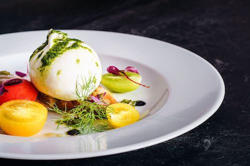 Burrata aux tomates jaunes et au basilic sur une assiette blanche, accord fromage du cocktail Passion des îles du Domaine de La Garnaudière