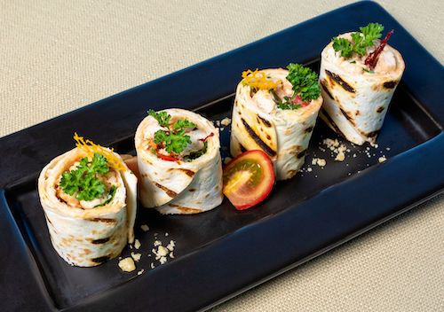 Wraps roulés aux herbes sur un plat noir, accord mets pour le cocktail Alizée bleue du Domaine de La Garnaudière
