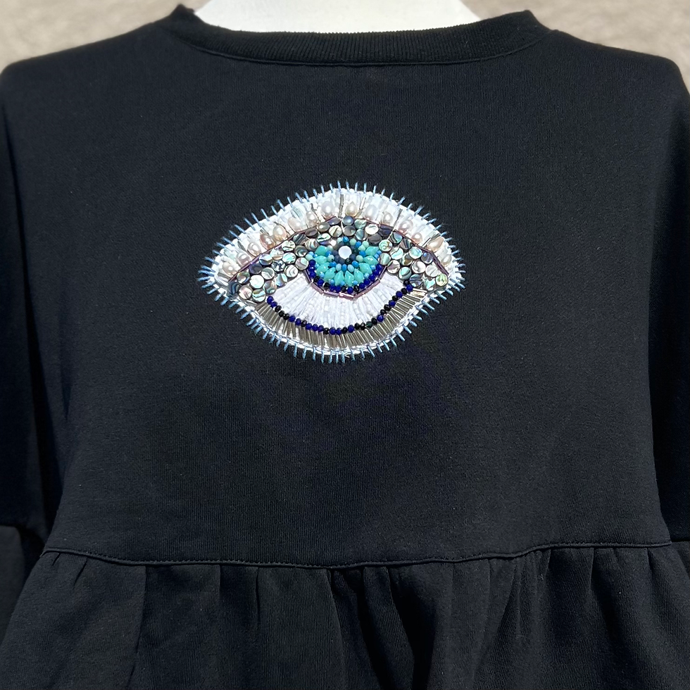 Hand embroidered evil eye patch made from pearls, beads, and cotton thread on peplum style crewneck sweatshirt