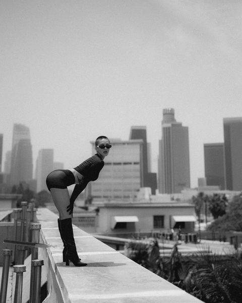 Woman in boots poses on rooftop ledge overlooking cityscape