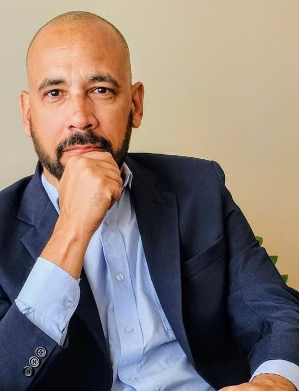 Homem careca com barba, terno e mão no queixo