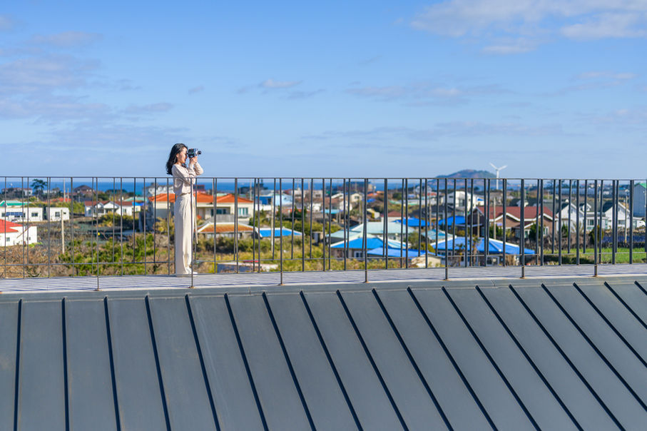 옥상 전망대에서 제주 마을과 바다를 내려다보는 여행자