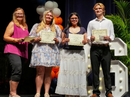 Four high school seniors standing and smiling with scholarship certificates