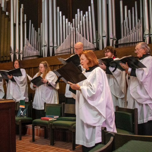 choir in white robes singing in front of pipe organ