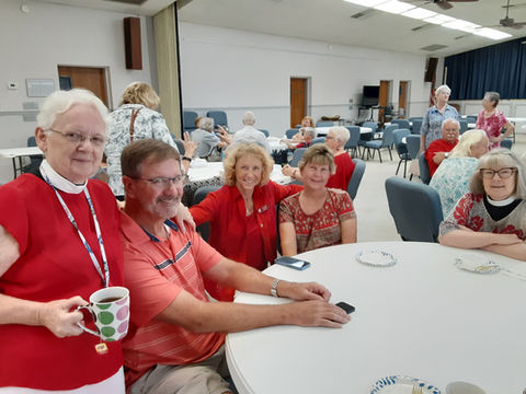 Group of people in fellowship hall standing and sitting at a table