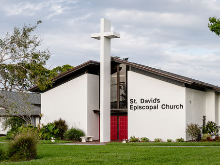 white church building with red doors and a large white cross in front taller than the building.