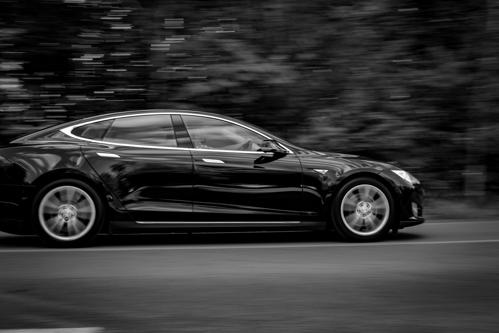 A black Tesla electric car with new tires driving fast on a road in front of a blurry background