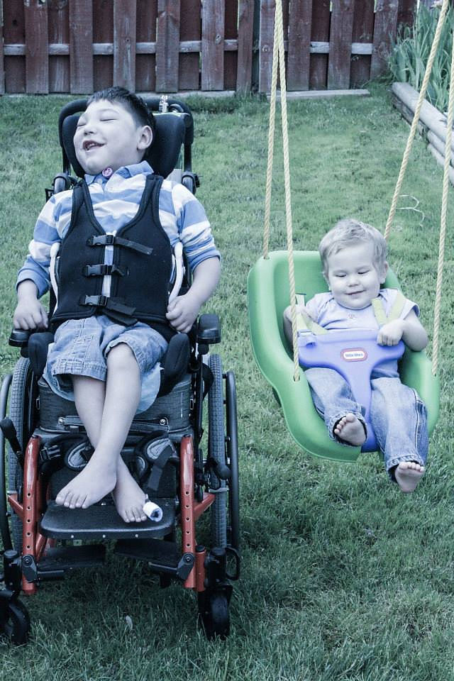 Image of Bret Bigelow outdoors with his sibling on a swing beside him.