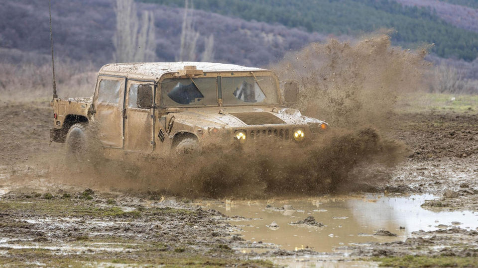 HMMWV vehicle travels through a puddle of dirt