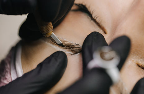 Hands in black gloves hold the manipulator with the microblading needle and draw her hair