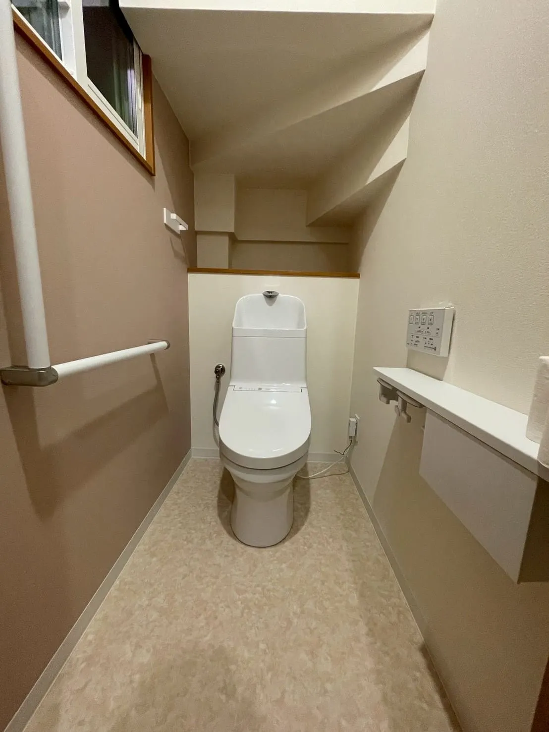ピンクの壁に白いトイレを設置した、階段下スペースのトイレ