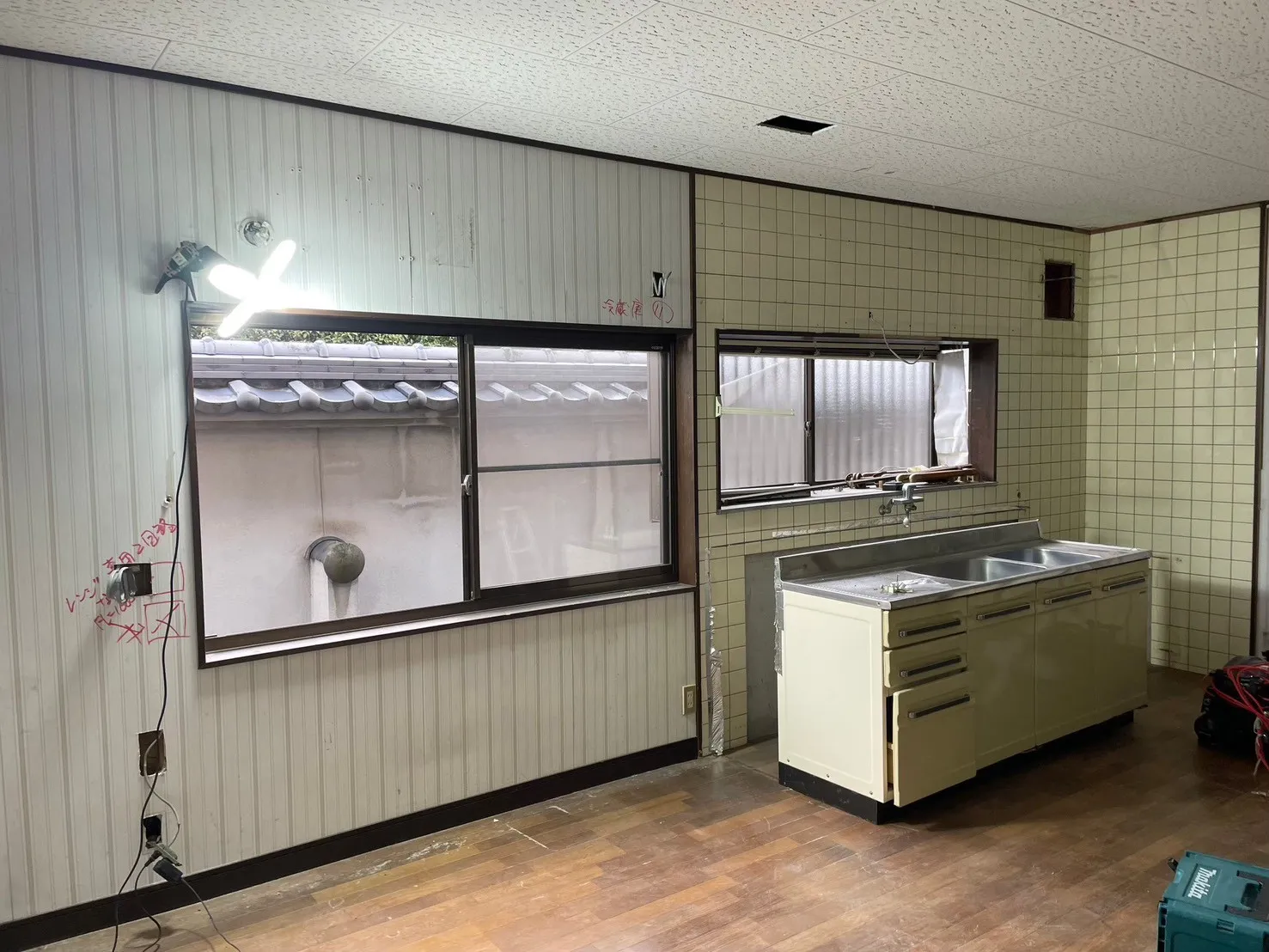 施工前のキッチン。黄緑色のタイル壁と旧式のステンレスシンクが残る解体中の状態