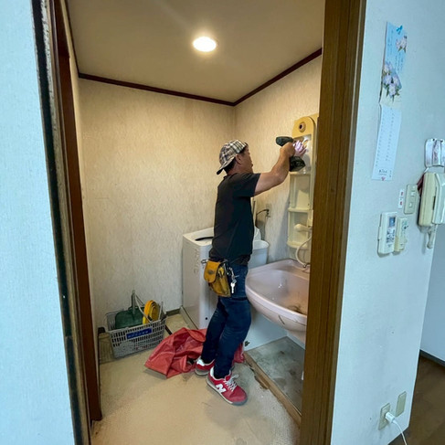 洗面・トイレエリアの撤去作業中。職人が旧洗面台の三面鏡を取り外している様子