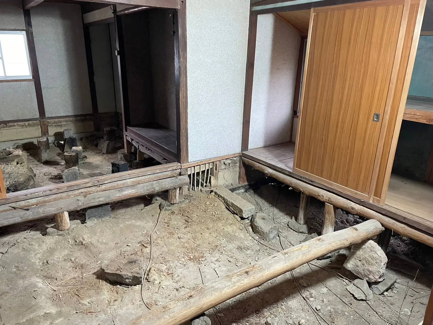 床板・畳を全て撤去した室内。石場建ての束石と大引きが並ぶ古民家の床下構造が広範囲に露わになった状態