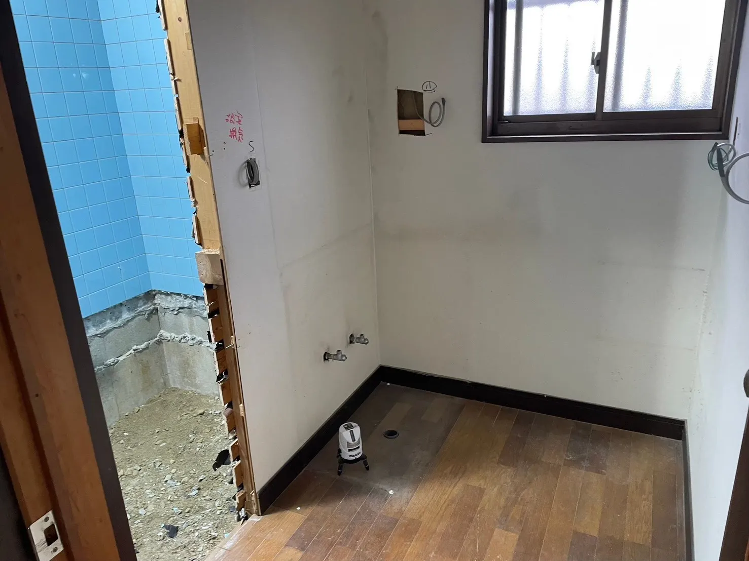 浴室を解体し、洗面脱衣室との間仕切り壁、左に水色タイルの浴室跡、右に脱衣室スペースが見える
