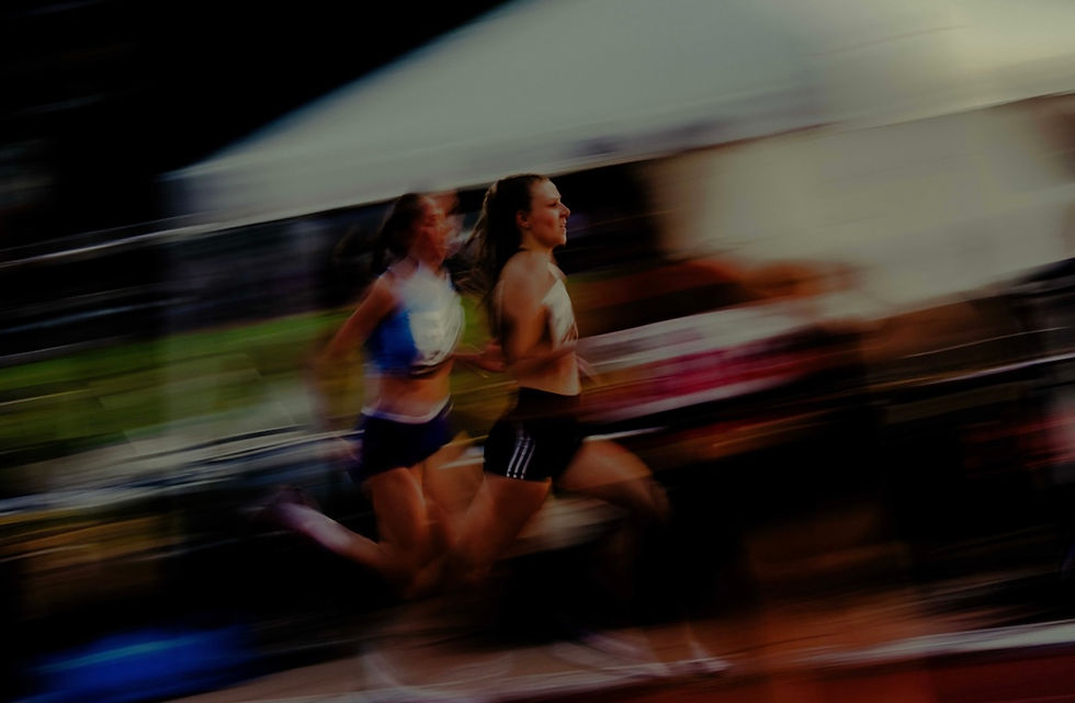 Two women sprint in a race, blurred motion in a stadium setting. They wear athletic gear, exuding focus and speed against a dynamic background.