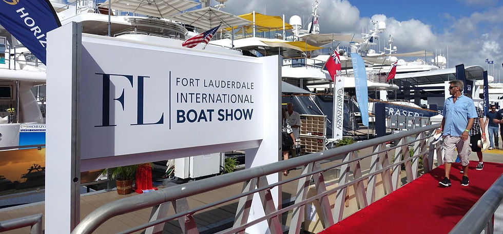 Man walks on red carpet at Fort Lauderdale International Boat Show. Yachts, flags, and blue sky in background create a vibrant scene.
