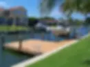 Dock with moored boat on canal, lined with palm trees and green lawn. Houses in the background under a clear blue sky.