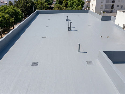 Foto aérea de una azotea plana de edificio residencial recién impermeabilizada con membrana Hyperdesmo gris, con los sumideros tratados y los encuentros con los petos perfectamente sellados. Iluminación natural de mediodía. Transmite resultado final limpio y técnicamente correcto.