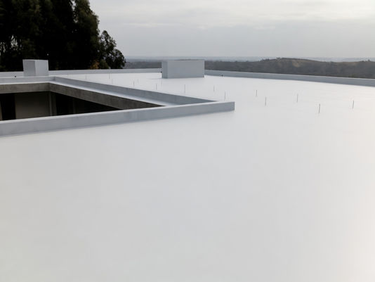 Foto de membrana líquida Hyperdesmo con rodillo sobre una terraza con baldosas existentes en buen estado. La membrana líquida blanca cubre las baldosas directamente. Iluminación natural exterior. Transmite que la obra es limpia, sin demolición y rápida.