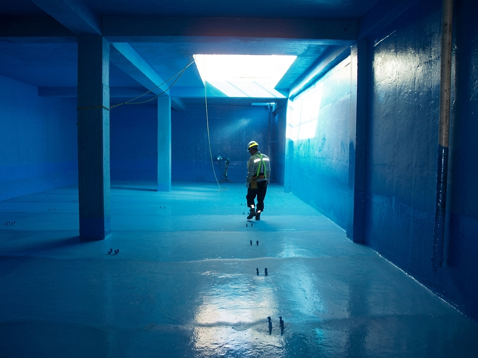Foto del interior de un depósito de agua potable vacío con el revestimiento interior de color gris azulado aplicado en toda la superficie — suelo, paredes y uniones. Iluminación artificial interior. Escala grande, ambiente técnico. Transmite la especificidad de la aplicación.
