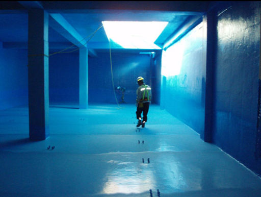 Foto del interior de un depósito de agua potable vacío con el revestimiento interior de color gris azulado aplicado en toda la superficie — suelo, paredes y uniones. Iluminación artificial interior. Escala grande, ambiente técnico. Transmite la especificidad de la aplicación.
