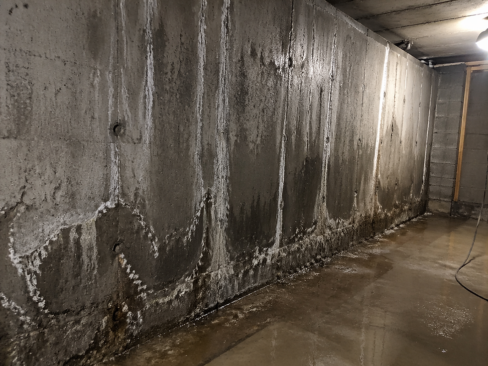 Foto del interior de un sótano o muro de contención con manchas de humedad y eflorescencias blancas visibles en el hormigón — el agua está entrando desde el exterior. Iluminación interior artificial. Transmite el problema técnico real de la presión hidrostática desde fuera.