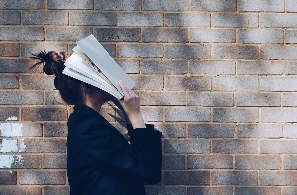 A stressed college student with a textbook covering her face