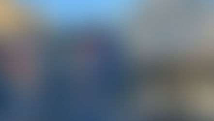 A wide street view of the Prince of Wales pub on Gloucester Road with its large colourful mural featuring flowers and a hummingbird. To the right is the Little Waitrose store with a modern glass frontage. The newly installed yellow defibrillator cabinet is mounted on the blue side wall of the pub.