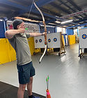 Alex Nelson holds a bow, aiming at a target