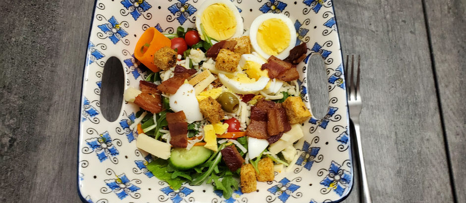 A beautiful salad with croutons, bacon chunks, halved eggs,  olives and smoky cheese