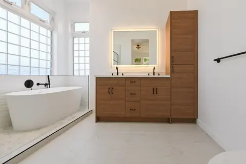 Modern minimalist bathroom with wood double vanity, freestanding tub, matte black fixtures, and frosted glass block windows – Green Bay Remodeling