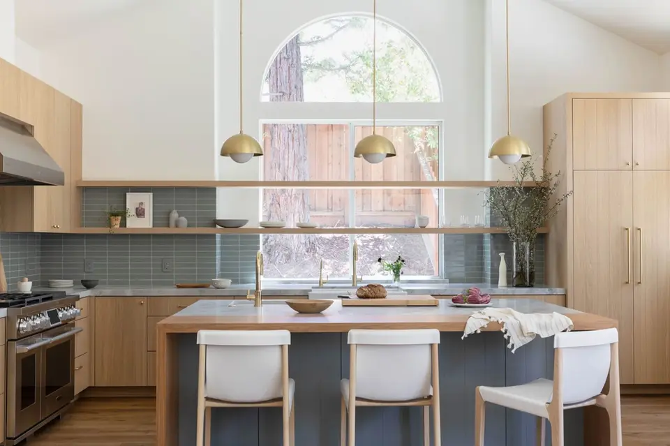 Modern Scandinavian-style kitchen with light wood cabinets, open shelving, gold pendant lights, and a large arched window – Green Bay Remodeling