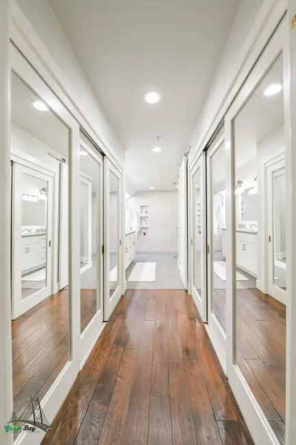 Upscale walk-in closet with mirrored sliding doors and hardwood flooring leading into a bright white double vanity bathroom – Green Bay Remodeling