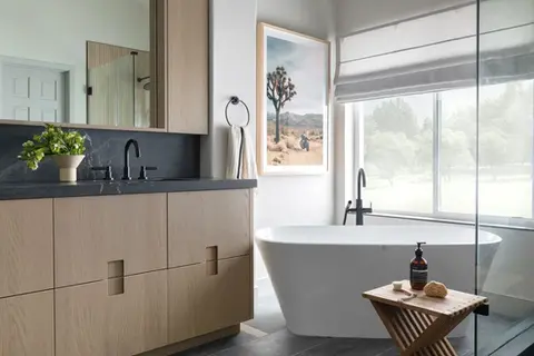 Modern bathroom with black stone vanity, light wood cabinets, freestanding soaking tub, and large window with natural light – Green Bay Remodeling
