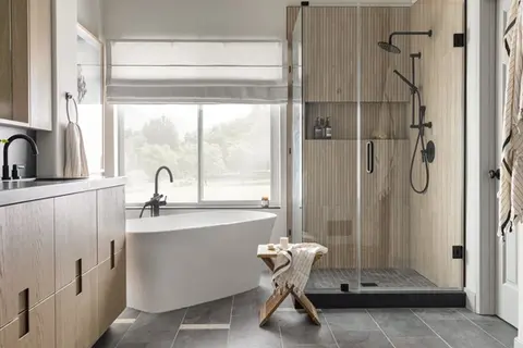 Modern bathroom with wood slat shower, black fixtures, freestanding tub, and natural wood vanity under soft daylight – Green Bay Remodeling