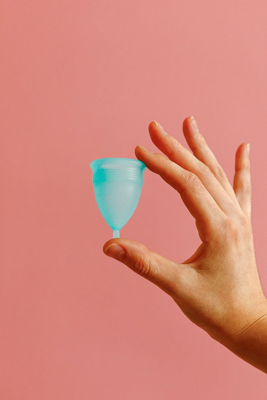 Hand holding a blue menstrual cup against a pink background, highlighting the contrast and delicate handling.