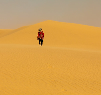 A lone woman hikes up a sand dune into the distance in the Namib desert..jpg