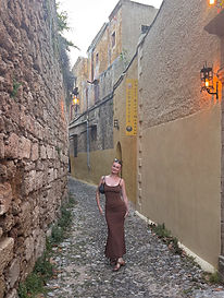 Cailin in a brown dress standing on a cobblestone street in Greece.