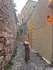 Cailin in a brown dress standing on a cobblestone street in Greece.